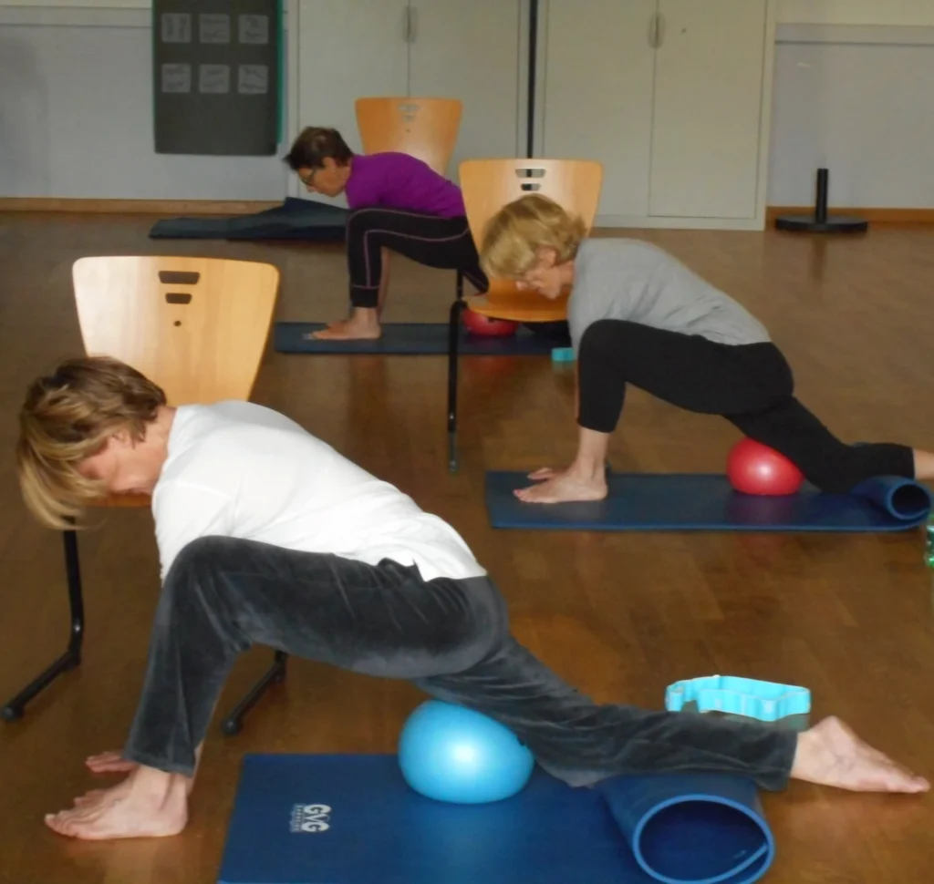 Trois femmes pratiquant le yoga en position de fente basse avec des ballons d'exercice sous les genoux.