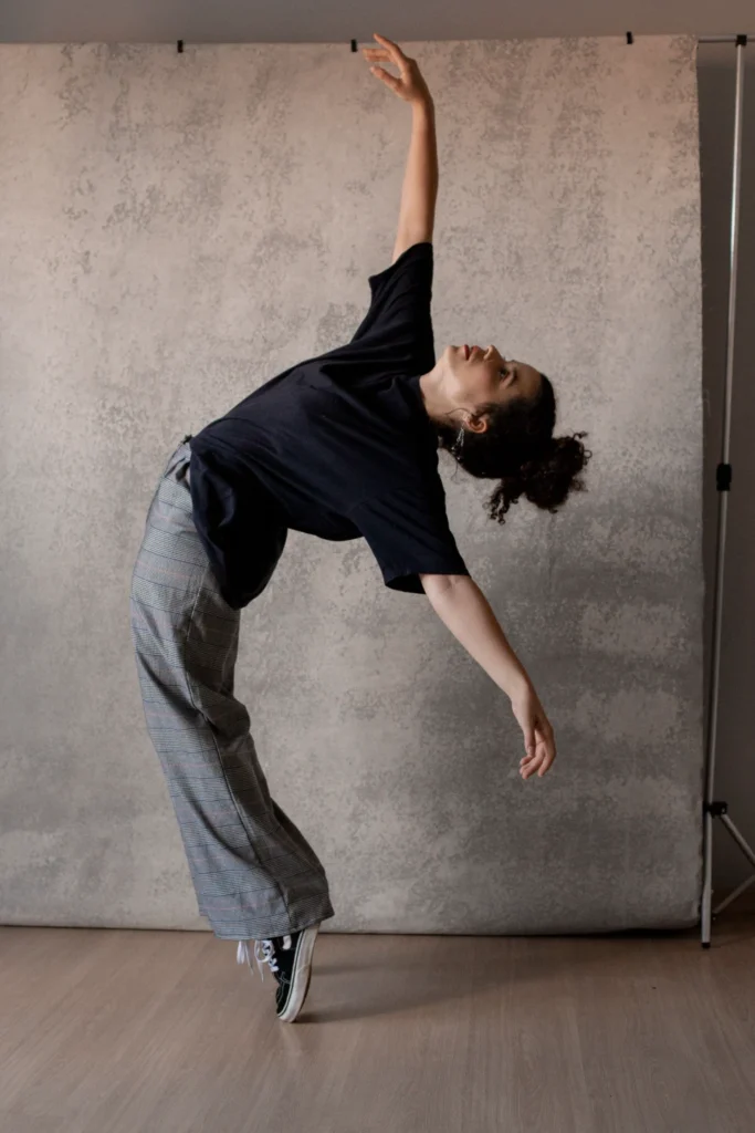 Danseuse se courbant en arrière, un bras levé, portant un haut noir et un pantalon à carreaux.