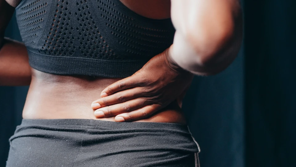 Une femme tenant son bas du dos, suggérant une douleur lombaire ou une gêne.