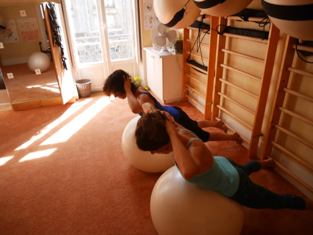Deux femmes allongées sur des ballons de Pilates, effectuant un exercice de renforcement du dos, mains derrière la tête.