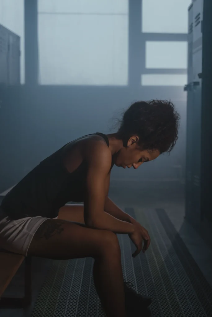 Femme assise sur un banc dans un vestiaire, tête baissée, visiblement fatiguée après un entraînement.