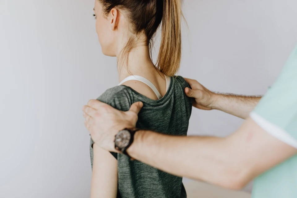 Un physiothérapeute manipule doucement l'épaule d'une femme vue de dos.